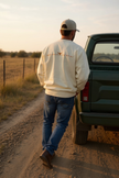 Un chandail ivoire à manches longues, coupe droite, avec l’inscription “REFINED COUNTRY” de couleur caramel au dos.
Entre les mots, un symbole de longhorn stylisé évoque l’esprit country chic propre à La-So Cowboy & Co.
Le design est minimaliste, moderne et raffiné.