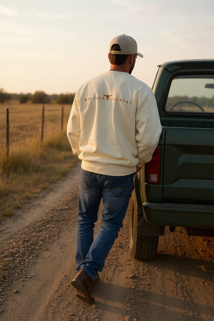 Un chandail ivoire à manches longues, coupe droite, avec l’inscription “REFINED COUNTRY” de couleur caramel au dos.
Entre les mots, un symbole de longhorn stylisé évoque l’esprit country chic propre à La-So Cowboy & Co.
Le design est minimaliste, moderne et raffiné.