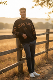 Un chandail noir à manches longues avec le texte de couleur caramel LA-SO COWBOY & CO. sur le devant et les manches. Le logo central LA-SO est surmonté d’un chapeau cowboy stylisé. Style affirmé et country chic.