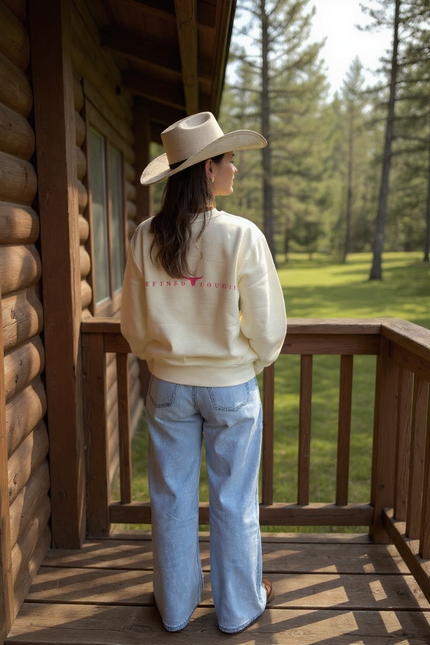 Un crewneck ivoire à manches longues, coupe droite, avec l’inscription “REFINED COUNTRY” en rose au dos.
Entre les mots, un symbole de longhorn stylisé évoque l’esprit country chic propre à La-So Cowboy & Co.
Le design est minimaliste, moderne et raffiné.